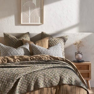 Bed with layered quilted bedding and patterned pillows against a textured wall framed geometric art hangs above
