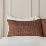 Bed with white sheets and brown quilted pillows against a beige paneled headboard creating a calm bedroom scene