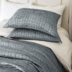 Close up of stacked gray quilted pillows on a light bedspread