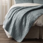 Close up of a blue quilted blanket folded over a white sheet on a wooden floor