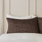 White pillows on a bed with a white sheet and a dark brown quilt beige paneled headboard in the background