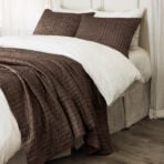Bed with white linens and brown quilted pillows arranged at the headboard in a neatly made bed   concise informative alt text