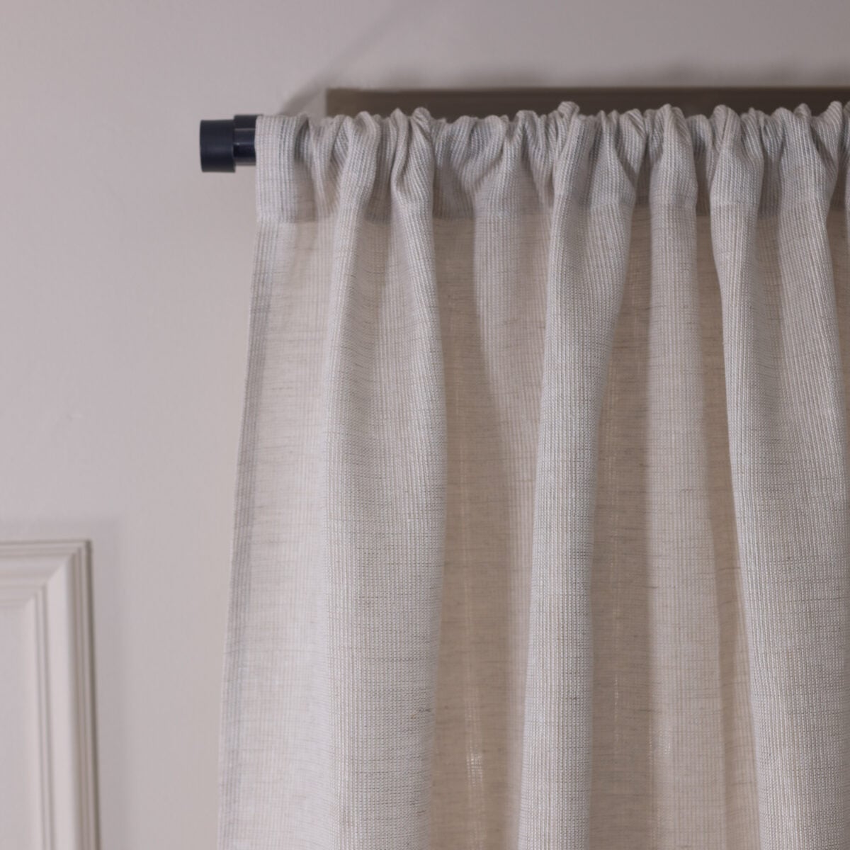 Light gray striped curtain gathered on a dark rod with a pale wall and door frame nearby