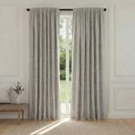 Light gray floor length curtains framing a glass door with a view of a green garden outside