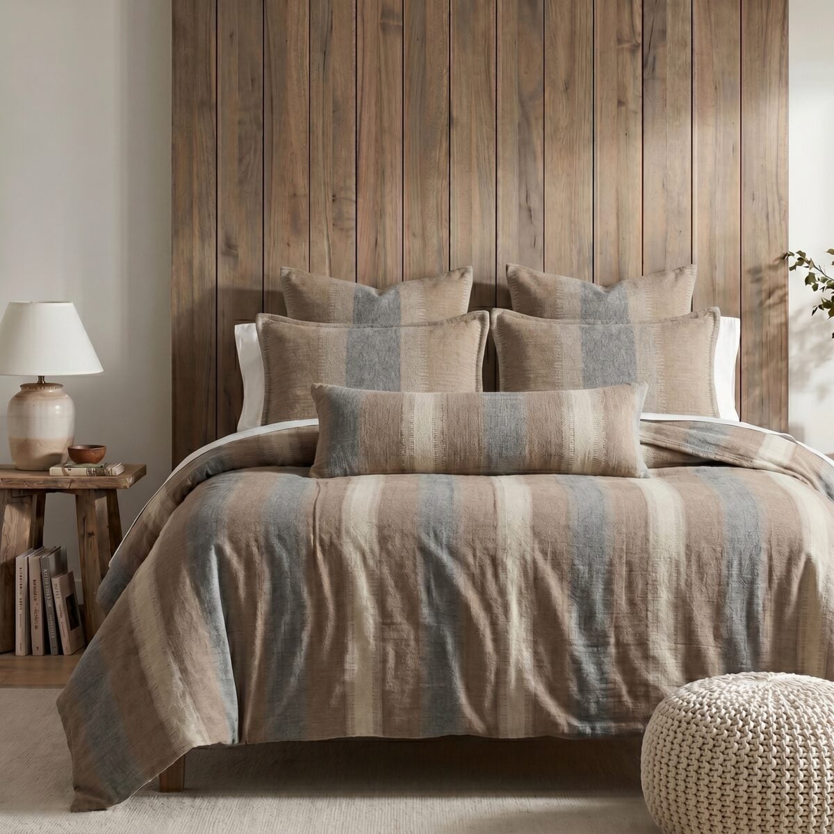 Cozy bedroom with a wooden paneled headboard neutral bed linens and matching pillows a lamp and small stack of books on a side table