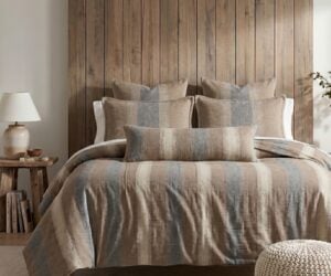 Cozy bedroom with a wooden paneled headboard neutral bed linens and matching pillows a lamp and small stack of books on a side table