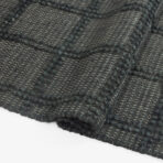Close up of dark gray woven fabric with thick yarns and diagonal texture patterns showing a boucle like weave