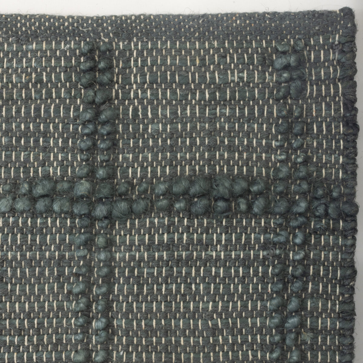 Close up of dark teal woven fabric with raised bobble stitches forming a dotted stripe pattern at regular intervals