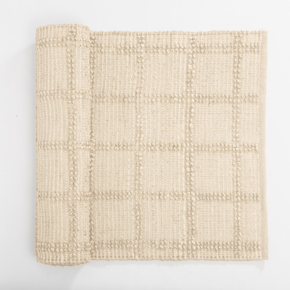 Beige woven textile close up with a dotted geometric pattern folded at the left edge on a white background