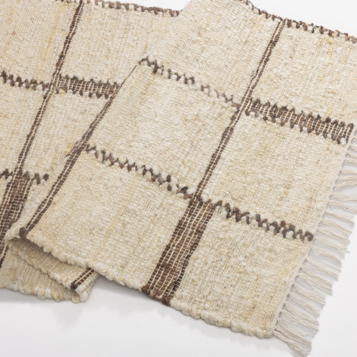 Close up of a cream woven rug with brown striped pattern and tassel fringe along the edge