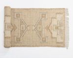 Beige woven rug with geometric diamond patterns and fringe along the right edge partially rolled at the left edge