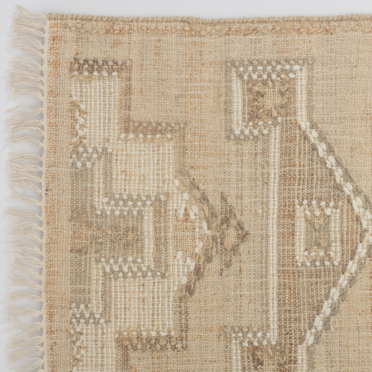 Beige woven rug with fringed edges along the left side and subtle patterning across the weave