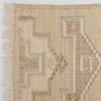 Beige woven rug with fringed edges along the left side and subtle patterning across the weave