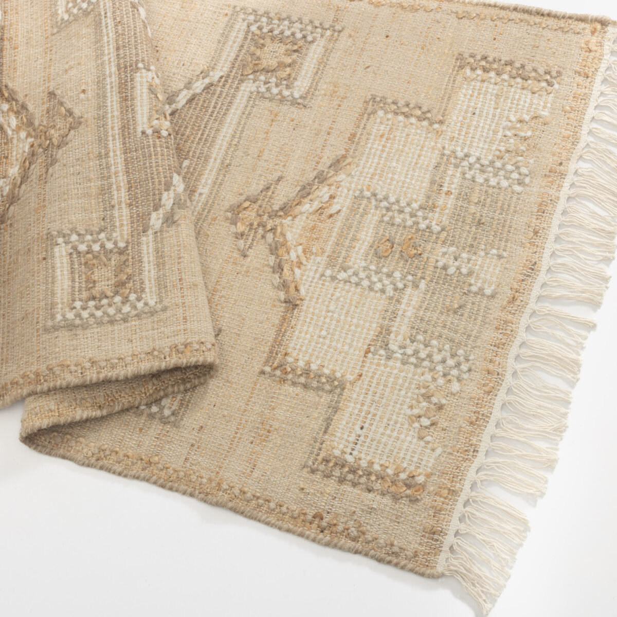 Close up of a beige woven rug with subtle geometric patterns and a fringed edge