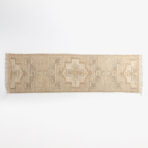 Beige woven rug with geometric square and diamond pattern and fringe along the bottom edge against a white background