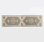 Top down view of a vintage beige rug with blue geometric diamonds and fringed edges on a white background