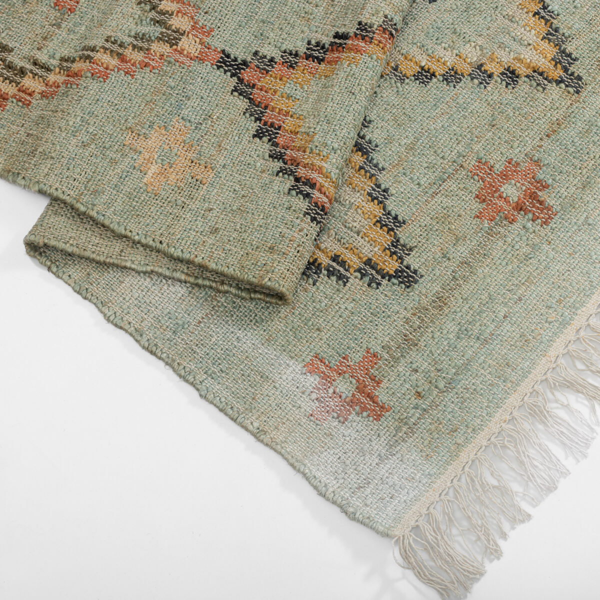 Folded woven rugs with fringe showing muted green cream and rust geometric patterns
