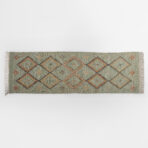 Edge of a woven rug with geometric diamond pattern on a light gray background fringe on sides