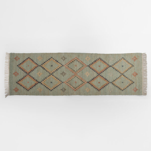 Edge of a woven rug with geometric diamond pattern on a light gray background, fringe on sides.