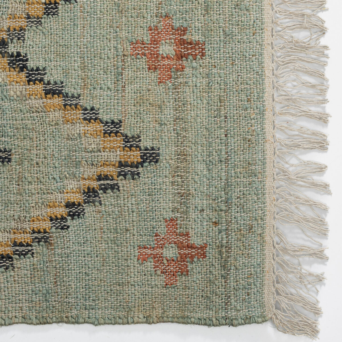 Close up of a woven rug with teal green threads mustard and black shapes and white fringe along the edge