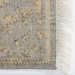 Close up of a gray and beige woven rug with textured knots and cream fringe on the right edge