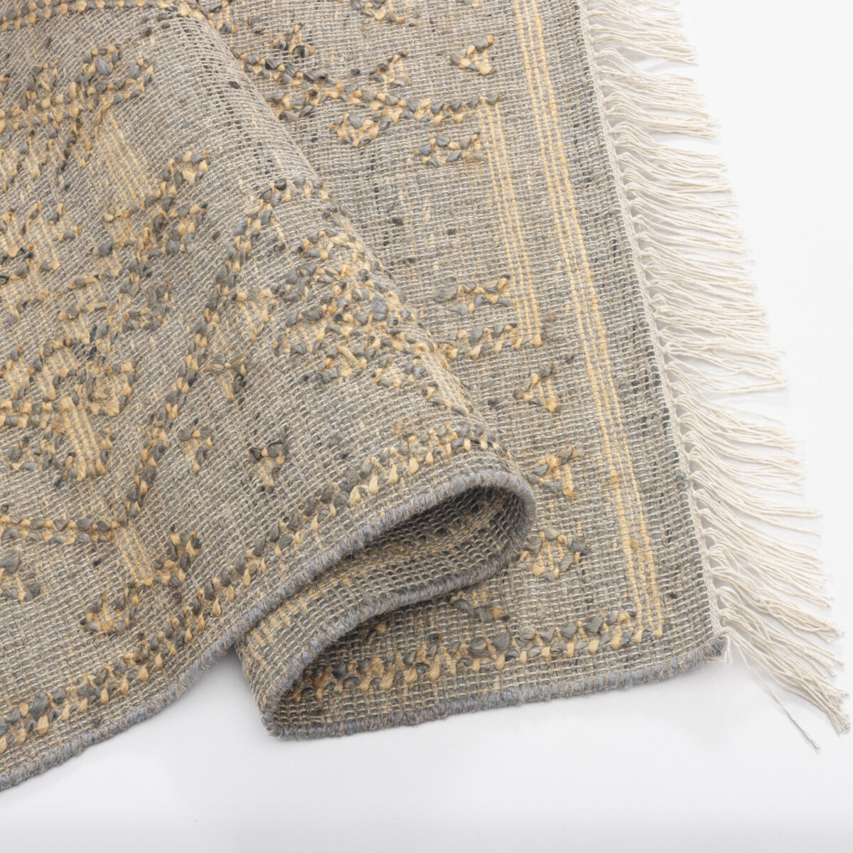 Folded textured woven rug in gray with beige accents and fringed edge on a white surface