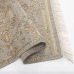 Folded textured woven rug in gray with beige accents and fringed edge on a white surface