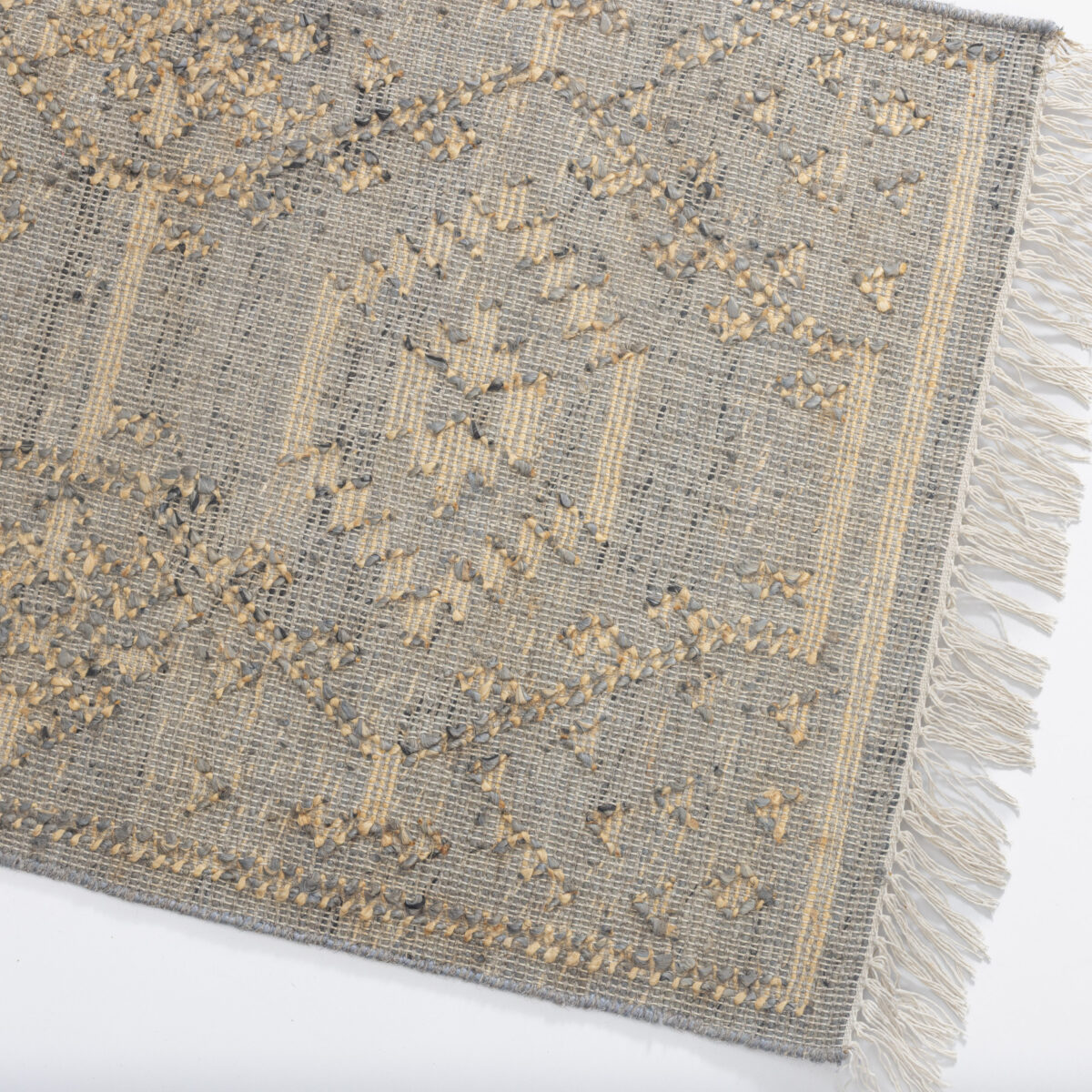 Close up of a textured gray woven rug with beige tassels along the edge and subtle patterning