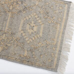 Close up of a textured gray woven rug with beige tassels along the edge and subtle patterning