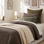 Cozy bedroom with olive green and gray pillows a quilted brown bedspread and botanical prints on the wall above the bed
