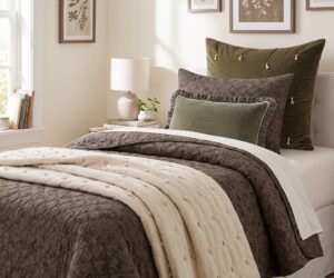 Cozy bedroom with olive green and gray pillows a quilted brown bedspread and botanical prints on the wall above the bed