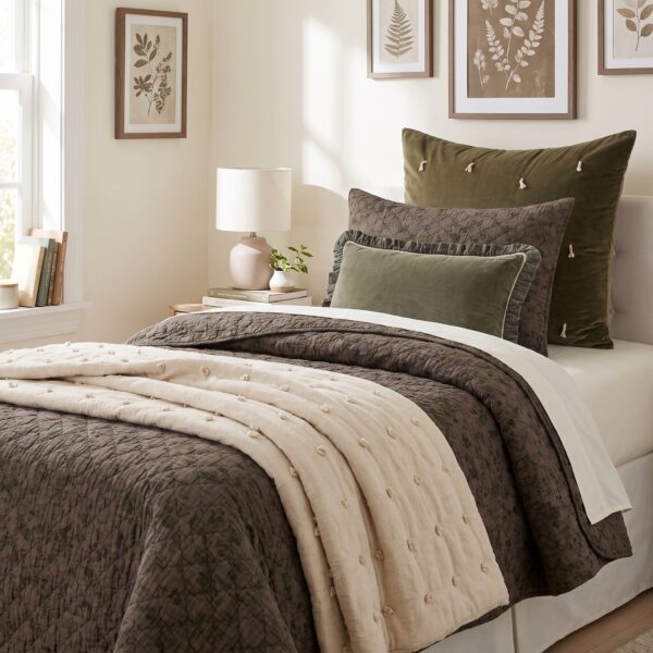 Cozy bedroom with olive green and gray pillows a quilted brown bedspread and botanical prints on the wall above the bed