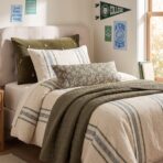Twin bed with cream headboard green velvet pillow striped bolster and university posters on the wall nearby