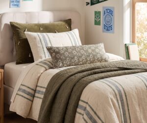 Twin bed with cream headboard green velvet pillow striped bolster and university posters on the wall nearby