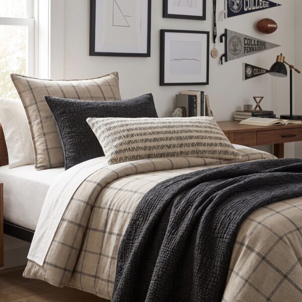 Bed with beige plaid duvet a black textured pillow and layered cream pillows in a cozy bedroom scene