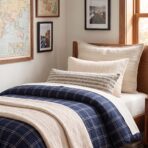 Bed with cream and striped pillows navy plaid bedding in a sunlit bedroom with map framed art on the wall