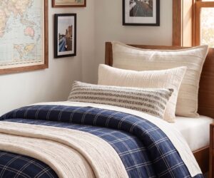 Bed with cream and striped pillows navy plaid bedding in a sunlit bedroom with map framed art on the wall