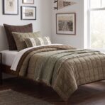 Bed with brown and beige quilted bedding and pillows framed wall art and a large window to the right