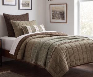 Bed with brown and beige quilted bedding and pillows framed wall art and a large window to the right