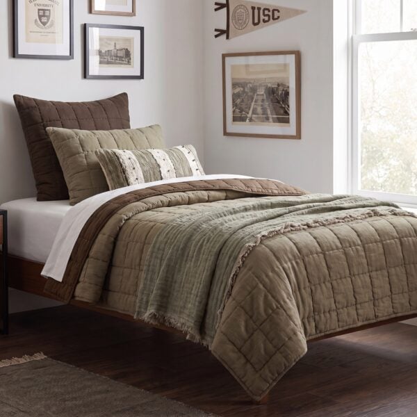 Bed with brown and beige quilted bedding and pillows framed wall art and a large window to the right