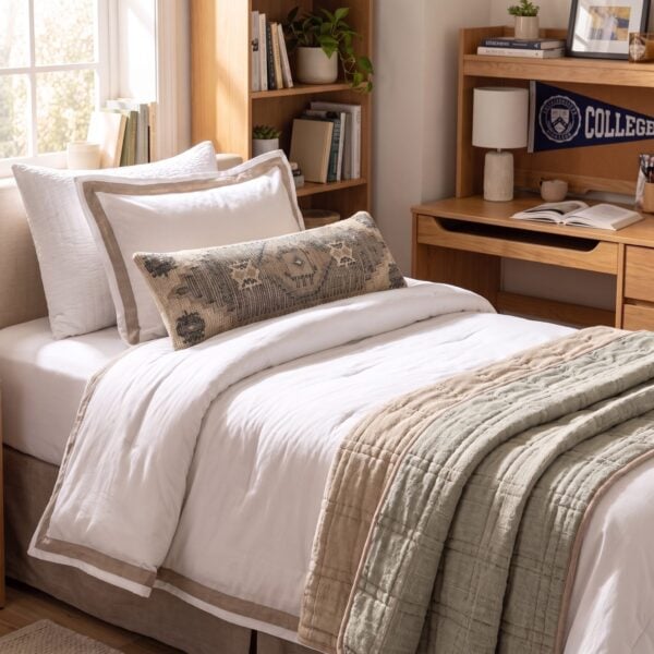 Cozy bedroom scene with a made bed white pillows and a beige quilt beside a wooden bookcase filled with books and plants
