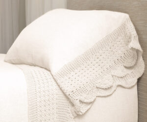 Cream knitted blanket draped over a light beige sofa close up of textured crochet pattern and soft fabric folds