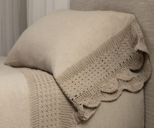 Close up of a beige crocheted throw laid over a light brown sofa showing a cozy texture