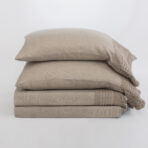 Stack of beige cushions with a knit beige throw draped along the right edge on a light background