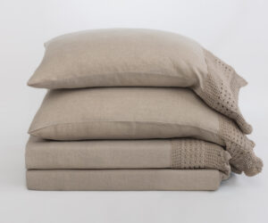 Stack of beige cushions with a knit beige throw draped along the right edge on a light background