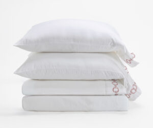 Stack of white pillows with smooth pillowcases arranged in a neat tower on a white background with a hint of pink pattern on the edge of the fabric on the right side