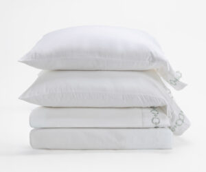 Stack of three white pillows stacked on a white surface with soft shadows and a crumpled pillowcase edge visible on the right side