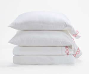 Stack of white pillows stacked in a bright minimal setting with packaging showing red lettering on the side