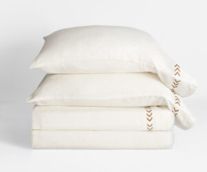 Stack of white pillows stacked in a neat pile with a brown chevron stitched edge on the right against a light background