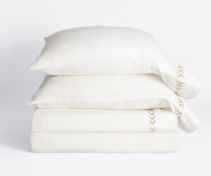 Stack of white pillows layered on top of each other against a pale background showing a brown chevron trim on the right edge of the top pillow